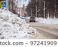 A large, high snowdrift against the backdrop of a city street with cars.  97241909