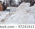 A huge, dirty snowdrift against the backdrop of a city street with cars.  97241913