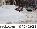 A large snowdrift against the backdrop of a city street with cars. 97241924
