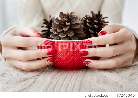Woman's hands with red manicure and gold foil on the nails. Trendy autumn and winter nail design. Woman with a beautiful manicure holding a red knitted cup. The concept of cozy Christmas holidays. 97243049