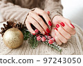 Female hands with red manicure and gold foil on the nails. Winter and Christmas time concept. Manicured woman's hands with Christmas decoration. 97243050