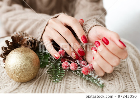 Female hands with red manicure and gold foil on the nails. Winter and Christmas time concept. Manicured woman's hands with Christmas decoration. Female hands with red manicure and gold foil on the nails. Winter and Christmas time concept. Manicured woman's hands with Christmas decoration. 97243050