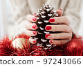 Female hands with red manicure and gold foil on the nails. Winter and Christmas time concept. Manicured woman's hands with Christmas decoration. 97243066
