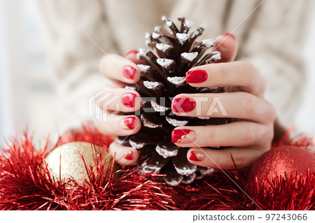 Female hands with red manicure and gold foil on the nails. Winter and Christmas time concept. Manicured woman's hands with Christmas decoration. Female hands with red manicure and gold foil on the nails. Winter and Christmas time concept. Manicured woman's hands with Christmas decoration. 97243066