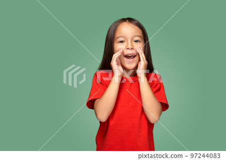 Portrait of a small pretty girl standing sideways and calling someone holding her hand near her mouth 97244083