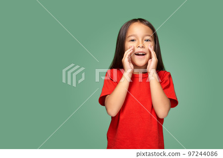 Portrait of a small pretty girl standing sideways and calling someone holding her hand near her mouth 97244086