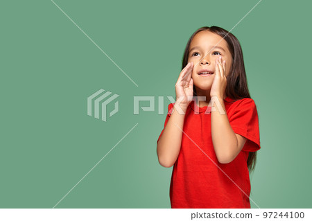 Portrait of a small pretty girl standing sideways and calling someone holding her hand near her mouth 97244100