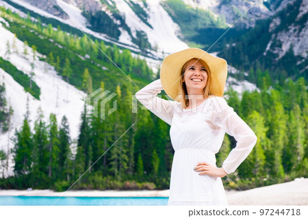 Smiling woman in summer hat and white dress against Dolomites Alps and Braies Lake. Smiling woman in summer hat and white dress against Dolomites Alps and Braies Lake. 97244718