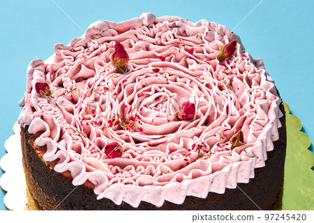 Delicious pink cream cake decorated with a small dried rosebuds, standing on a gold stand against a blue studio background. 97245420