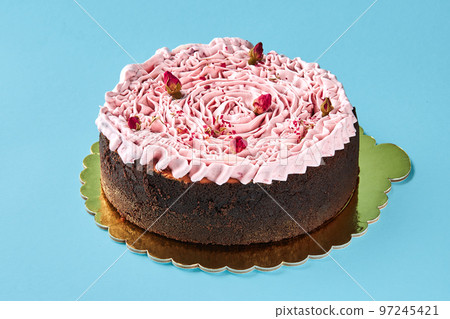 Delicious pink cream cake decorated with a small dried rosebuds, standing on a gold stand against a blue studio background. 97245421