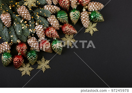 Green branches of a Christmas tree with decorations in the form of golden, red, green cones and snowflakes on a black background with twinkling festive lights with a place for text. Top view Green branches of a Christmas tree with decorations in the form of golden, red, green cones and snowflakes on a black background with twinkling festive lights with a place for text. Top view 97245978