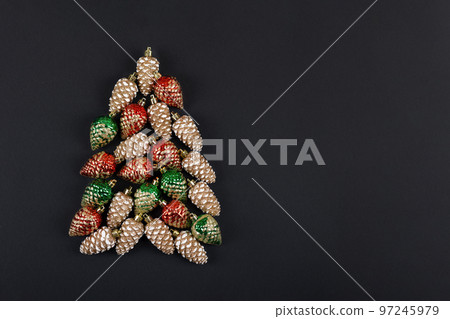 Christmas tree composition of tree decorations in the form of pine cones in red green and gold on black background with a place for text 97245979