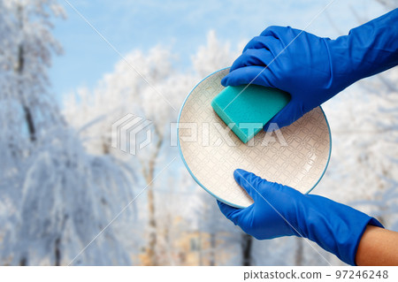Women's hands in protective gloves with sponge and plate with winter on background. Women's hands in protective gloves with sponge and plate with winter on background. 97246248