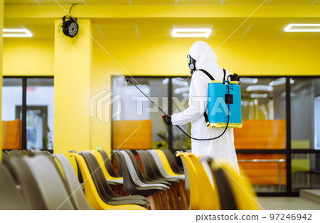 Man wearing protective suit disinfecting assembly hall with spray. Disinfecting of office. COVID-19. 97246942