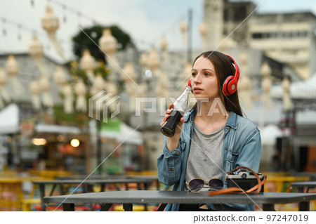 Attractive female traveller drinking cola from glass bottle while sitting at outdoor street food restaurant Attractive female traveller drinking cola from glass bottle while sitting at outdoor street food restaurant 97247019