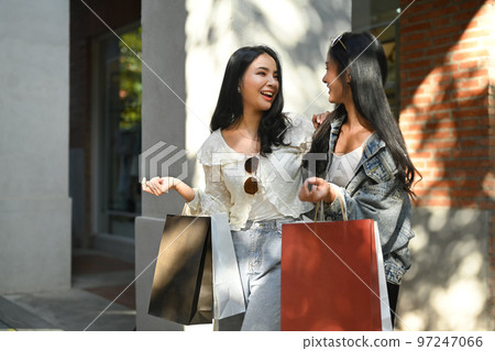Two cheerful women doing shopping together, talking, gossiping at city streets on sunny day Two cheerful women doing shopping together, talking, gossiping at city streets on sunny day 97247066