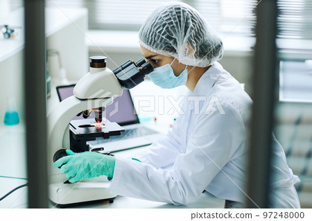Young female technician looking in microscope working in lab 97248000