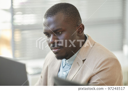 Close up black man looking at computer screen while working in office cubicle 97248517