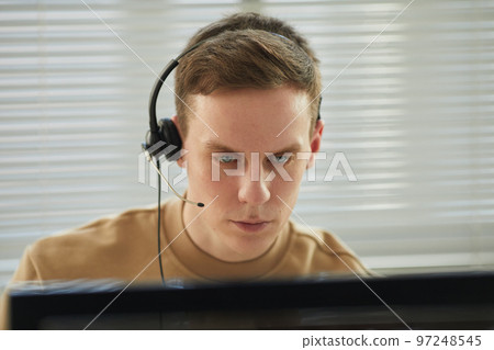 Young man wearing headset in tech support office Young man wearing headset in tech support office 97248545