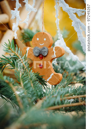Wooden gingerbread man with felt grey bow and ruby buttons on green pine branch. Street decorations in Colmar market in Alsace 97249267