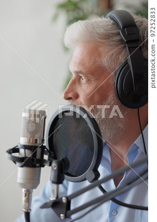 older man with gray hair irecording podcast in recording studio with microphone and headphones older man with gray hair irecording podcast in recording studio with microphone and headphones 97252833