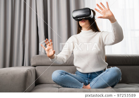 Young woman in vr glasses, playing video games and touching something in the air. Playing games at home in the living room Young woman in vr glasses, playing video games and touching something in the air. Playing games at home in the living room 97253589