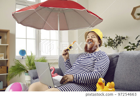 Funny happy fat man sitting on sofa and using laptop to book tickets for summer holiday Funny happy fat man sitting on sofa and using laptop to book tickets for summer holiday 97254663