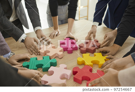 Team of young business people connecting colorful parts of jigsaw puzzle on table Team of young business people connecting colorful parts of jigsaw puzzle on table 97254667