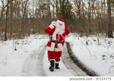 Santa Claus is walking near forest white background covered in snow while carrying red bag full of gifts for children presents 97254775