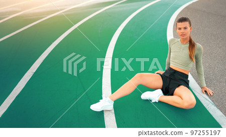 Tired happy woman runner taking rest after run sitting running track 97255197