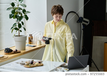 Young photographer connecting camera with laptop to watch her photos during shooting in studio 97255883