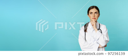 Young female doctor, hospital worker in white coat, thinking and looking away thoughtful, searching solution, standing over toquoise background 97256139