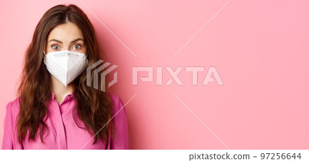 Covid-19, quarantine and social distancing concept. Close up of young stylish woman with nice hairdo, wearing medical respirator from coronavirus, pink background Covid-19, quarantine and social distancing concept. Close up of young stylish woman with nice hairdo, wearing medical respirator from coronavirus, pink background 97256644