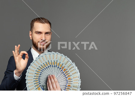 Handsome young smart businessman showing OK gesture with us dollars banknotes fan Handsome young smart businessman showing OK gesture with us dollars banknotes fan 97256847