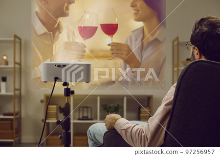 Lonely man is relaxing at home in evening watching romantic movie on TV projector. 97256957