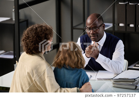 High angle portrait of young mother with child talking to caring black social worker in office 97257137