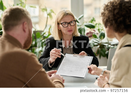 Portrait of mature woman handing contract forms to couple in legal services agency Portrait of mature woman handing contract forms to couple in legal services agency 97257156