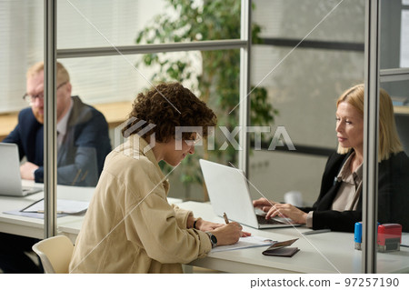 Side view portrait of young woman filling application form in consulate office Side view portrait of young woman filling application form in consulate office 97257190
