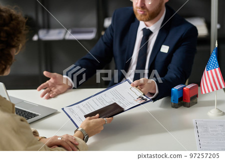 Close up of woman handing visa application form to worker in US embassy office 97257205