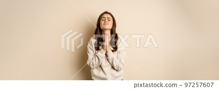 Woman begging and pleading god, supplicating, say please, standing desperate over beige background 97257607