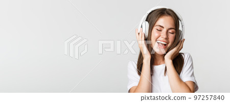 Close-up of attractive happy woman listening music in wireless headphones, singing along Close-up of attractive happy woman listening music in wireless headphones, singing along 97257840