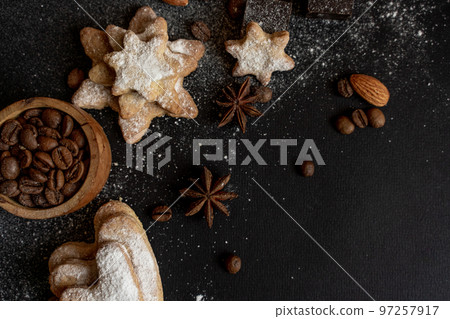 black background with homemade cakes, fragrant cookies. Cookies in the form of hearts, stars, coffee beans, spices, almonds close-up. the concept of the menu. Full size 97257917