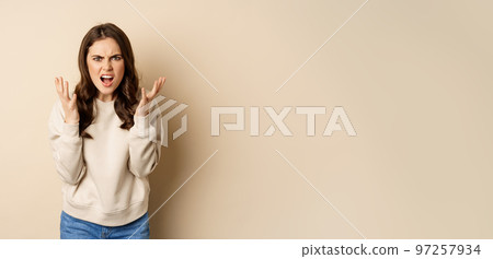 Angry frustrated woman arguing, shouting and yelling outraged, shaking hands furious, standing over beige background Angry frustrated woman arguing, shouting and yelling outraged, shaking hands furious, standing over beige background 97257934