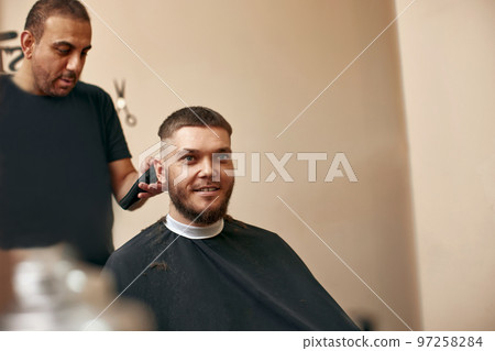 Barber shaving caucasian man in barber shop Barber shaving caucasian man in barber shop 97258284