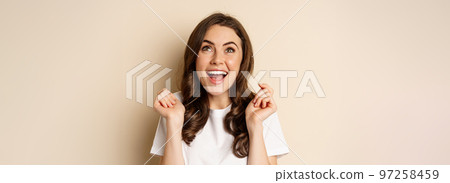 Close up portrait of enthusiastic young woman rejoicing, shouting with joy and satisfaction, celebrating victory, winning and triumphing, standing over beige background Close up portrait of enthusiastic young woman rejoicing, shouting with joy and satisfaction, celebrating victory, winning and triumphing, standing over beige background 97258459