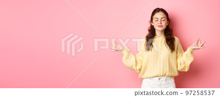 She is relaxed. Smiling young peaceful girl meditating, holding hands in zen gesture, close eyes, feel relieved and calm, standing against pink background She is relaxed. Smiling young peaceful girl meditating, holding hands in zen gesture, close eyes, feel relieved and calm, standing against pink background 97258537