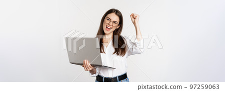 Enthusiastic office woman, businesswoman holding laptop and shouting with joy, celebrating and rejoicing, standing over white background Enthusiastic office woman, businesswoman holding laptop and shouting with joy, celebrating and rejoicing, standing over white background 97259063