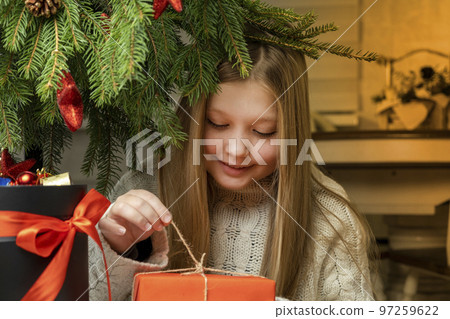Merry Christmas, happy holidays. Cheerful cute little blonde girl opens a Christmas present Merry Christmas, happy holidays. Cheerful cute little blonde girl opens a Christmas present 97259622