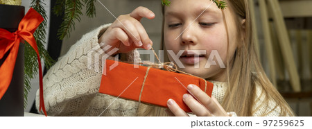 Merry Christmas, happy holidays. Cheerful cute little blonde girl opens a Christmas present 97259625