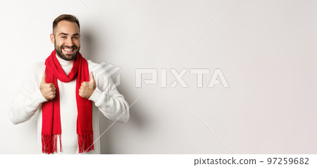 Winter holidays and shopping concept. Cheerful bearded man in red christmas scarf showing thumbs up, approve and recommend store, standing over white background 97259682